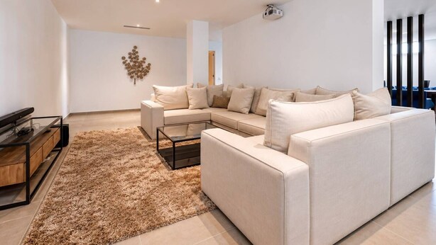 A modern living room with a sectional sofa, a coffee table, a TV, and a decorative wall piece. - The Solstice Estate – Private Pool Retreat for Families & Groups (Marbella)