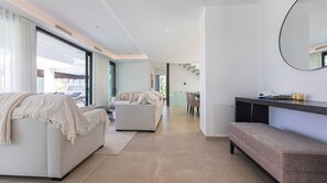 A modern living room with a sofa, a bench, and a dining area in the background. - The Solstice Estate – Private Pool Retreat for Families & Groups (Marbella)