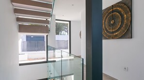 A modern interior with a glass staircase, a view to the outside, and a decorative wall piece. - The Solstice Estate – Private Pool Retreat for Families & Groups (Marbella)