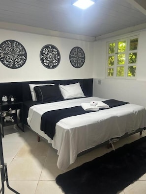 Un dormitorio con cama, mesita de noche, alfombra negra y decoración mural.