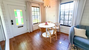 Ein Zimmer mit Holzboden, einem runden Tisch mit Stühlen, einem blauen Sofa und einem Fenster mit Vorhängen.