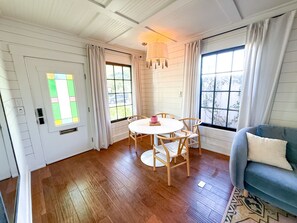 A room with a wooden floor, a round table with chairs, a blue sofa, and a window with curtains. - Rosé Chalet (San Diego)
