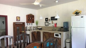 A compact kitchen with a dining area, wooden chairs, a white refrigerator, and a water dispenser. - Serene Lake Front Beach Cottage in charming Tela (Tela)