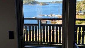 Vista de uma varanda com guarda-corpo de madeira, com vista para um corpo d'água, barcos e uma ilha ao longe.