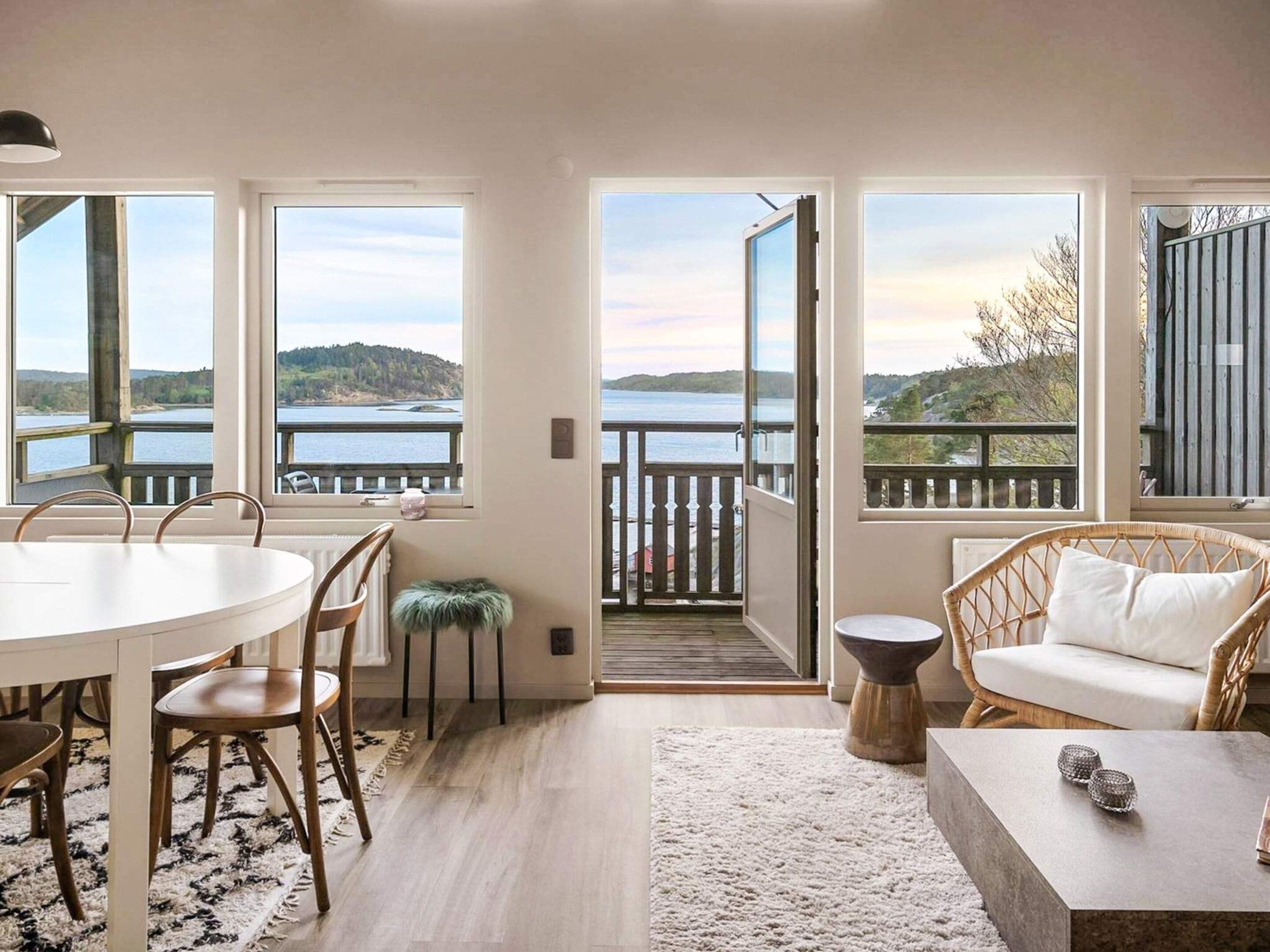 A room with a dining table, chairs, a sofa, and a view of a lake through large windows.