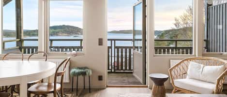 A room with a dining table, chairs, a sofa, and a view of a lake through large windows.