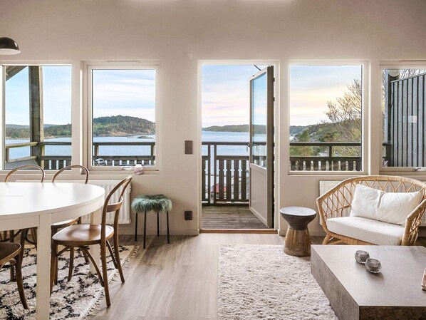 A room with a dining table, chairs, a sofa, and a view of a lake through large windows. - 5 Star Holiday Home in Uddevalla (Uddevalla)