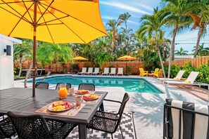 Un espace aménagé au bord de la piscine, comprenant une table à manger, des chaises, un parasol jaune et des chaises longues.