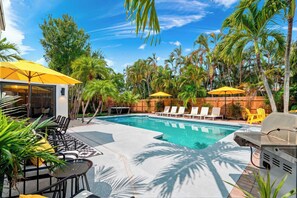 Un espace piscine équipé de chaises longues, d’un barbecue et de parasols.