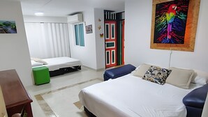 Quarto de hotel com cama, sofá, lixeira verde e um quadro colorido na parede.