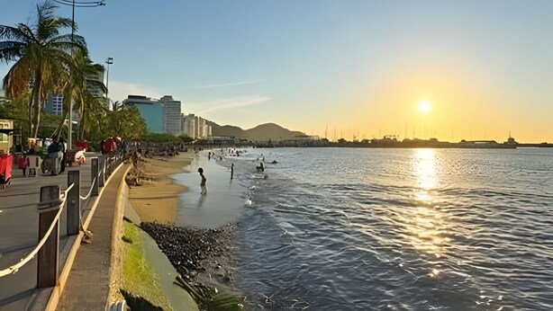 Uma praia com céu claro, pôr do sol e mar calmo.