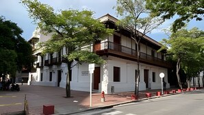 Um edifício de dois andares com fachada branca, varandas de madeira e um andar térreo de tijolos vermelhos.