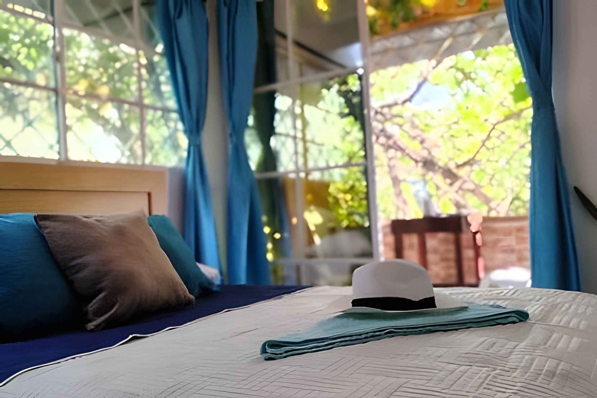 A bed with a white headboard, blue and brown pillows, and a folded hat on the bedspread.