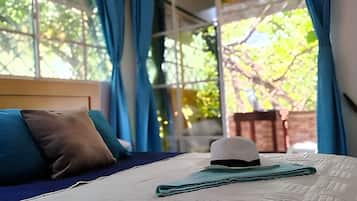 Un lit avec une tête de lit blanche, des oreillers bleus et bruns, et un chapeau plié posé sur le couvre-lit.