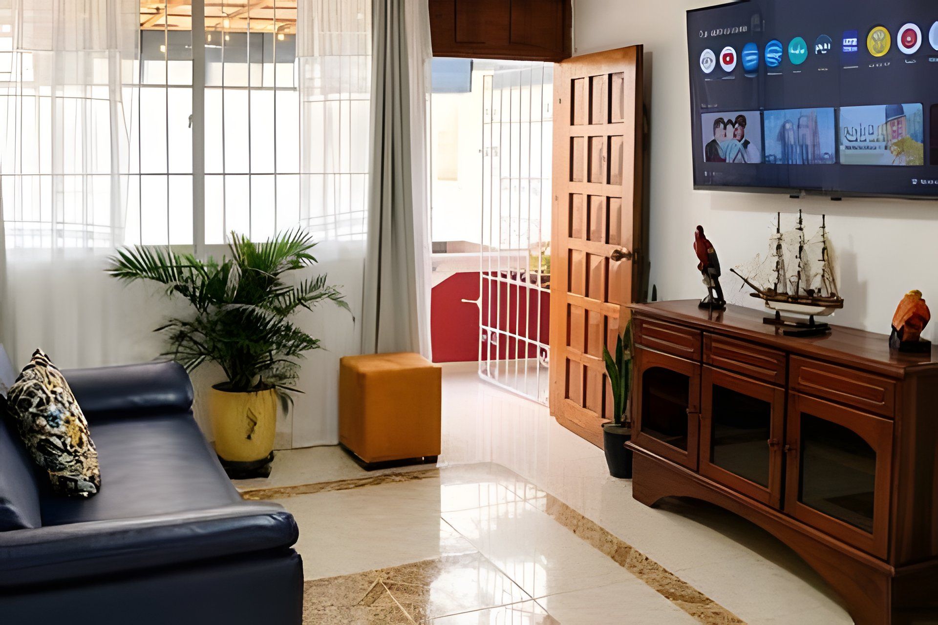 A living room with a sofa, a TV mounted on the wall, a wooden cabinet, and a potted plant.