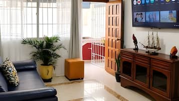 A living room with a sofa, a TV mounted on the wall, a wooden cabinet, and a potted plant.