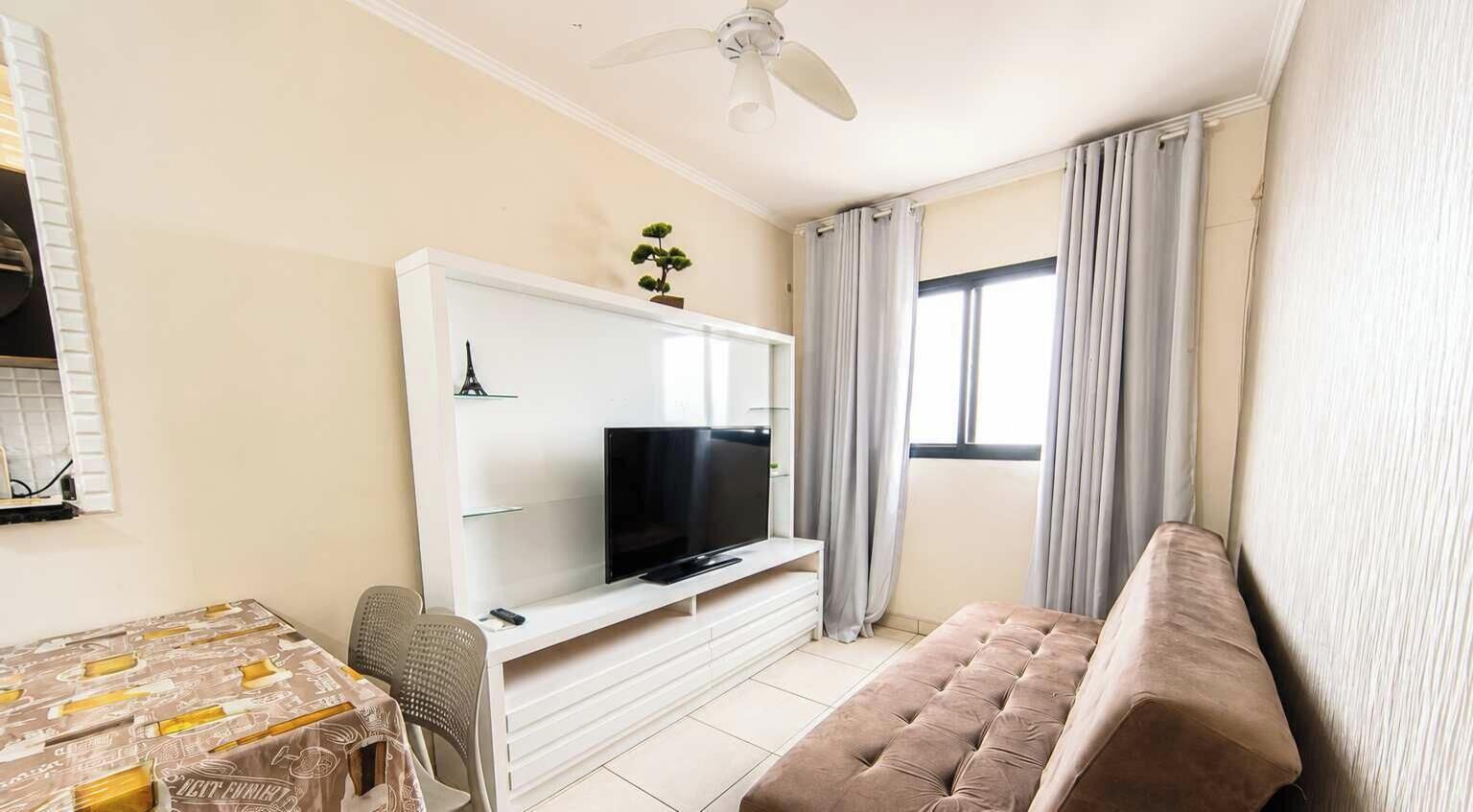 A living room with a flat-screen TV, a sofa, a dining table, and a ceiling fan.
