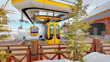 A yellow cable car suspended above a wooden deck with snow on the ground.