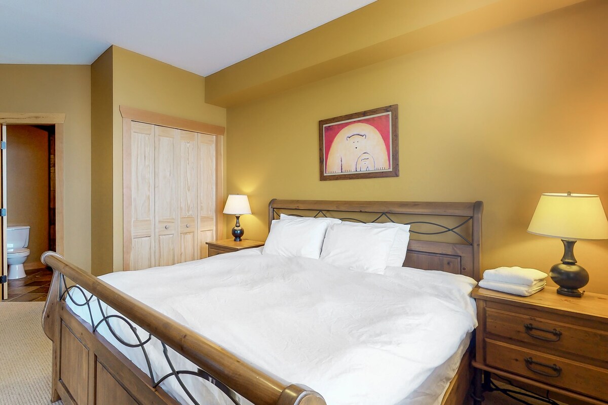 A neatly made bed with white linens, a wooden headboard, and two bedside lamps.