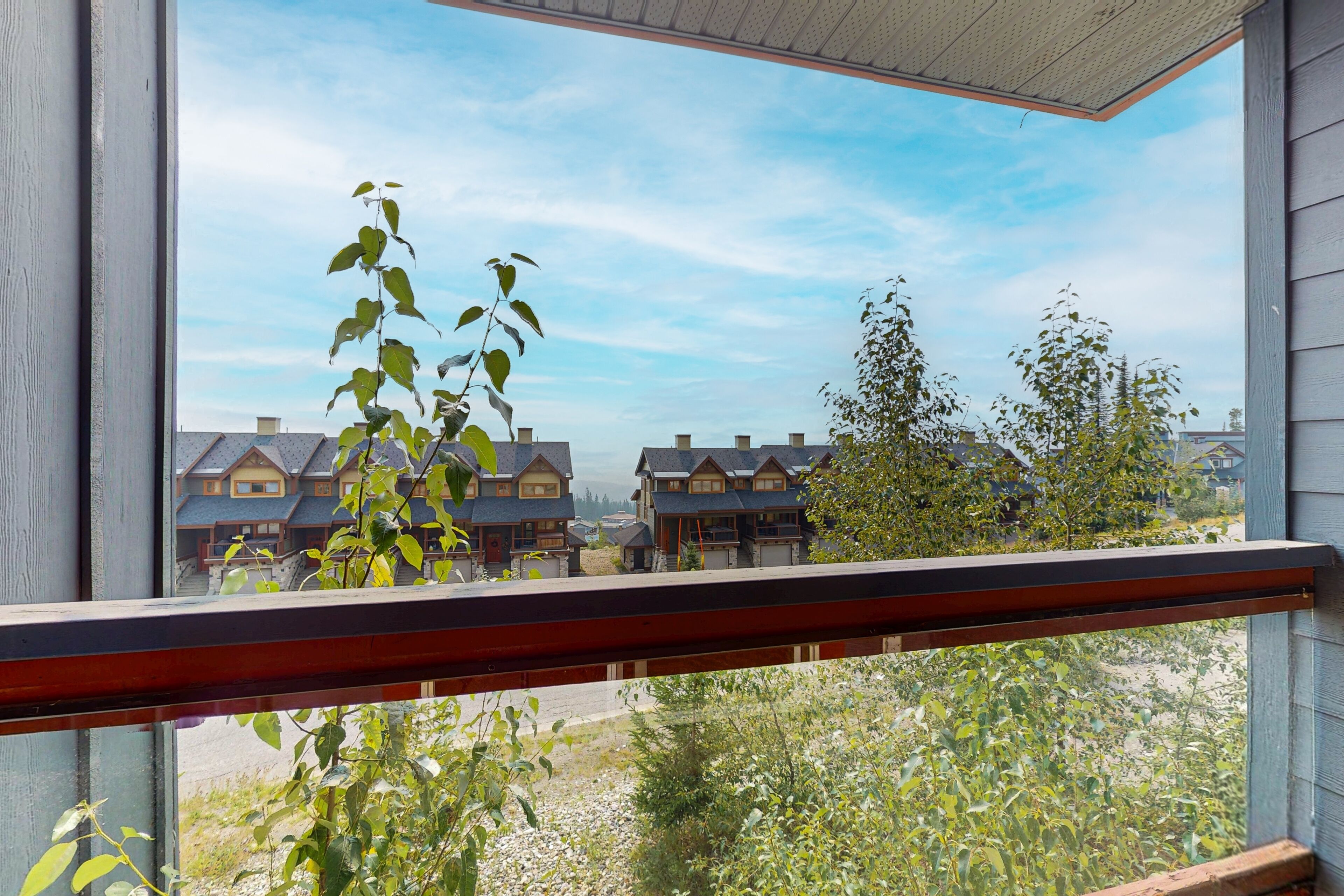 Une vue depuis un balcon doté d’une balustrade en bois, donnant sur une rangée de maisons à l’architecture similaire, avec un ciel dégagé.