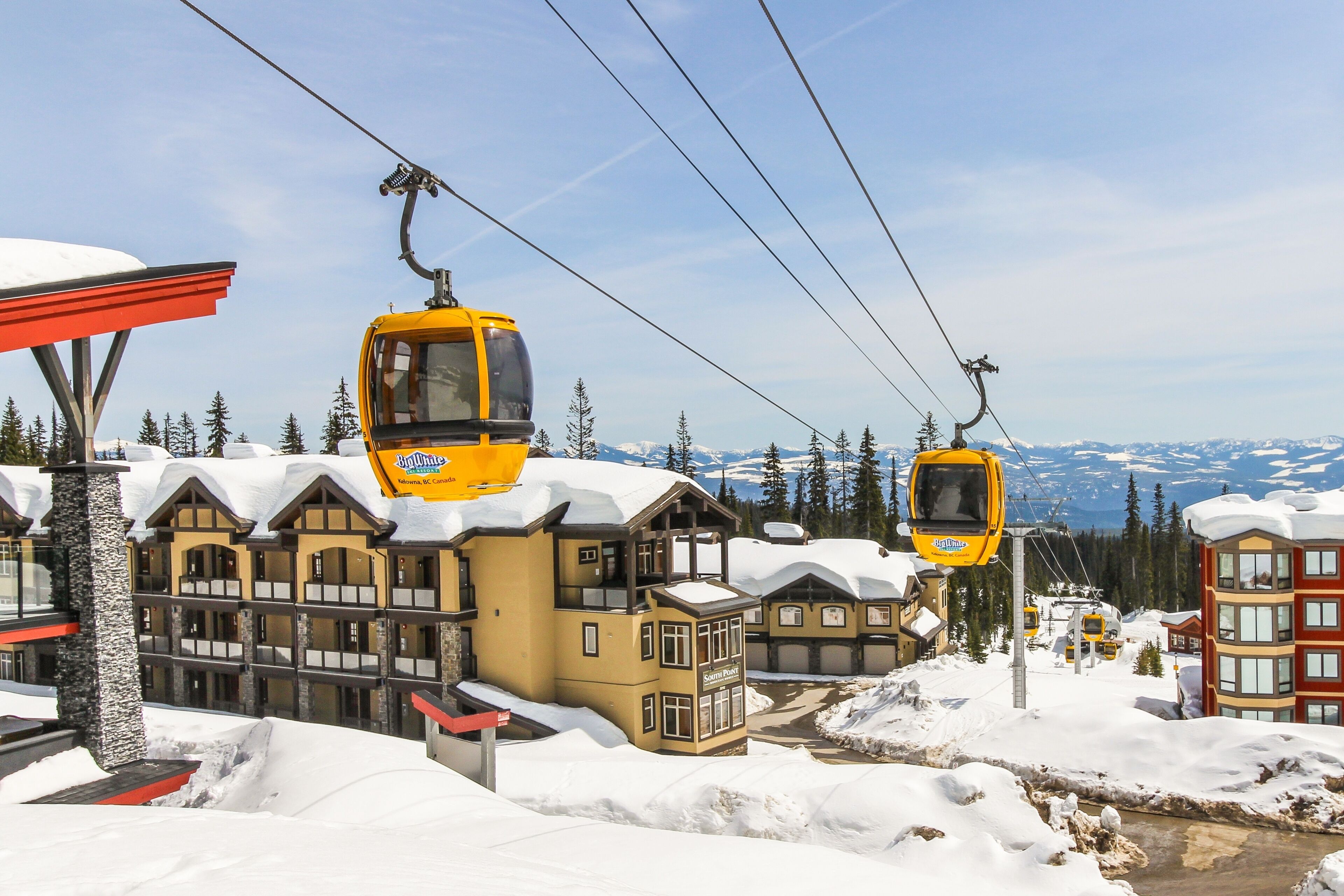 A ski resort with yellow cable cars, wooden buildings, and snow-covered mountains in the background.