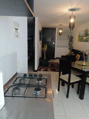 A modern kitchen with a gas stove, a dining area with a table and chairs, and a living room with a sofa and a painting on the wall. - Lindo Apartamento amoblado a minutos de sitios turisticos (Montenegro Province)