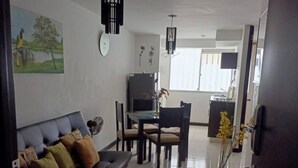Ein Wohnzimmer mit einer Couch, einem Esstisch mit Stühlen, einem Fernseher und einer Uhr an der Wand.