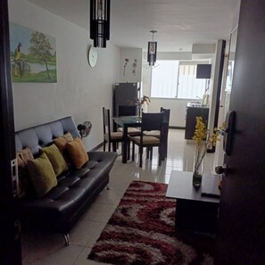 A living room with a sofa, a dining table with chairs, a TV, and a clock on the wall. - Lindo Apartamento amoblado a minutos de sitios turisticos (Montenegro Province)