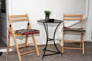 Two wooden chairs with woven seat covers, a small round table with a potted plant, and a white textured wall. - Traditional Cretan house in Limnes – 10 minutes from Agios Nikolaos. (Limne)