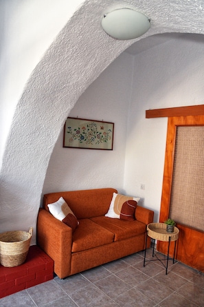 A cozy living area with a curved ceiling, a sofa, a small side table, and a decorative wall piece. - Traditional Cretan house in Limnes – 10 minutes from Agios Nikolaos. (Limne)