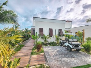 Un bâtiment moderne doté d’une allée pavée, d’une voiturette de golf et de plantes tropicales.