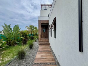 Un bâtiment moderne avec un escalier en bois menant à une porte, le tout entouré d’une végétation luxuriante et sous un ciel dégagé.