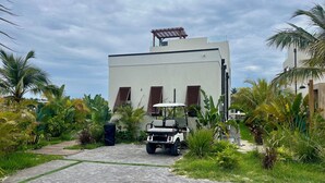 A modern building with a paved driveway, a golf cart, and lush tropical vegetation. - Luxury 2026 Waterfront Home w/ Yacht Dock + Rooftop (Freeport)