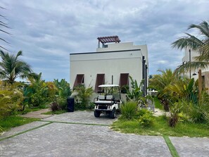 A modern building with a paved driveway, a golf cart, and lush tropical vegetation. - Luxury 2026 Waterfront Home w/ Yacht Dock + Rooftop (Freeport)