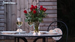 Una mesa con un jarrón de rosas rojas, dos copas de vino blanco y una vela.