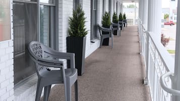 A covered walkway with benches and planters along the side of a building with large windows.