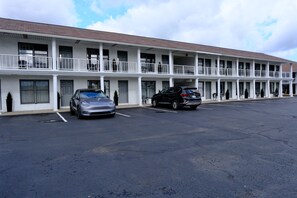 Un motel con una estructura de dos pisos, zona de estacionamiento techada y cielo despejado.