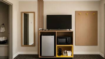 Une chambre d’hôtel équipée d’un téléviseur à écran plat, d’un mini-réfrigérateur, d’un four à micro-ondes et d’une machine à café, le tout posé sur une étagère en bois.
