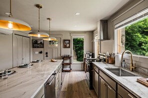 A modern kitchen with a marble countertop, pendant lighting, and a view of greenery outside. - Historic Hodge House|2BD•2BA|King Beds| Sleeps 6 (Banner Elk)