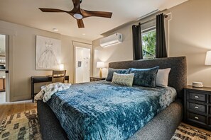 A bedroom with a bed, a ceiling fan, an air conditioning unit, a window with curtains, a bedside table, and a lamp. - Historic Hodge House|2BD•2BA|King Beds| Sleeps 6 (Banner Elk)