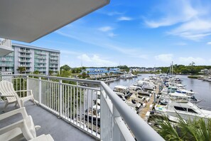 A balcony with white chairs, overlooking a marina with boats and a building with blue roofs. - Waterfront Condo | Harbourgate Marina Views (North Myrtle Beach)