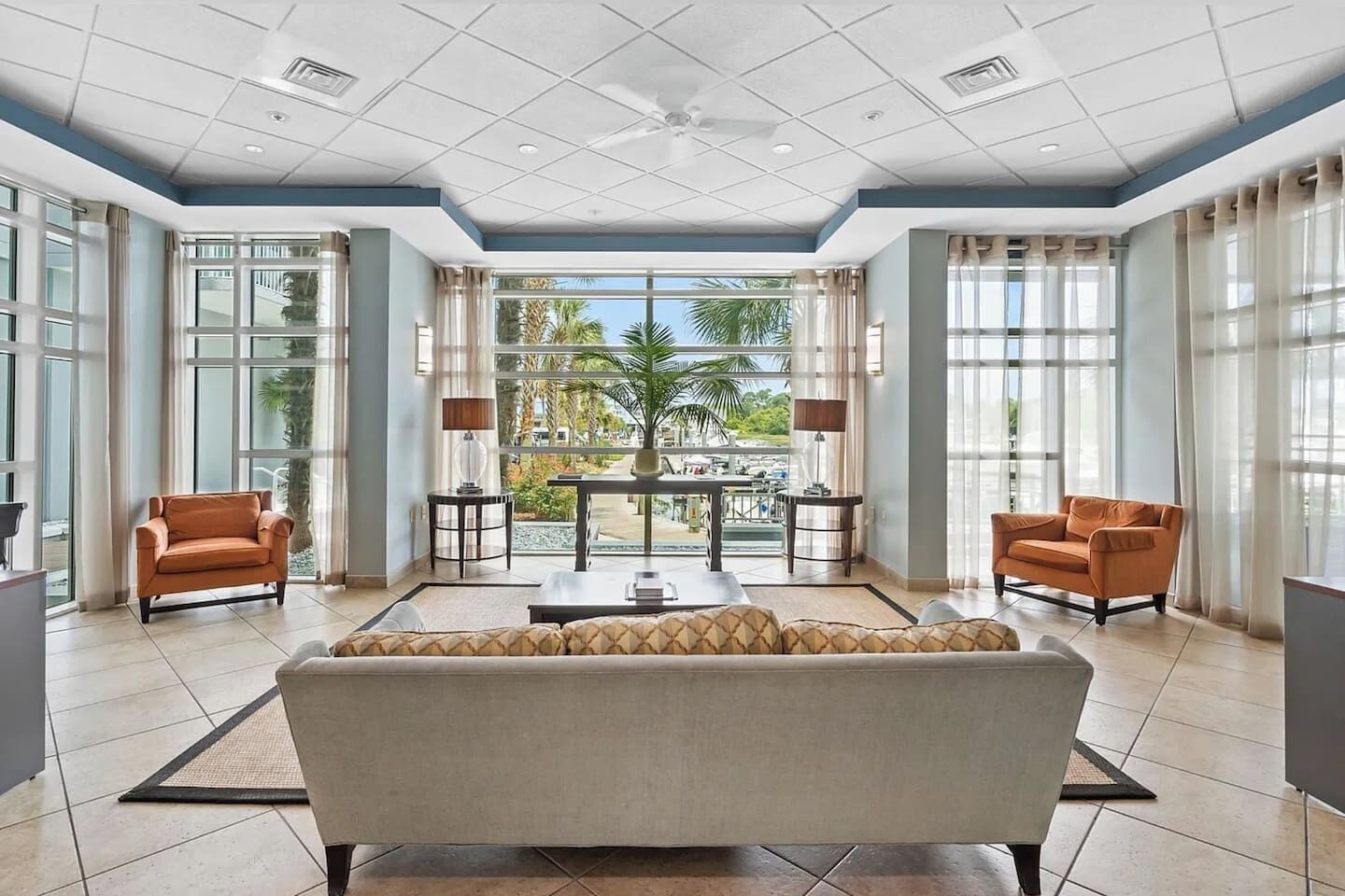 A spacious living area with a sofa, two armchairs, a coffee table, and a balcony with a view of palm trees.