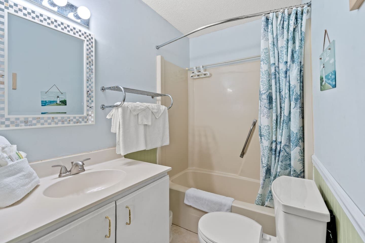 A bathroom with a sink, mirror, towel rack, shower, and toilet.