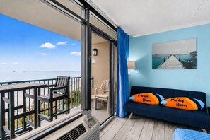 Ein Balkon mit Meerblick, eine Couch mit zwei Kissen, ein Sessel und ein Tisch.