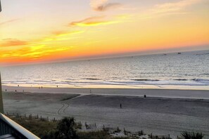 Ein Strand mit Sonnenuntergang, eine Sandfläche und einige Leute, die spazieren gehen.