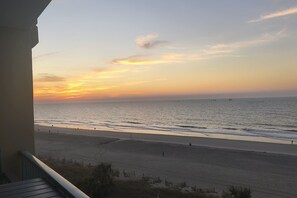 Blick auf einen Strand vom Balkon mit Geländer, Meer und blauem Himmel.