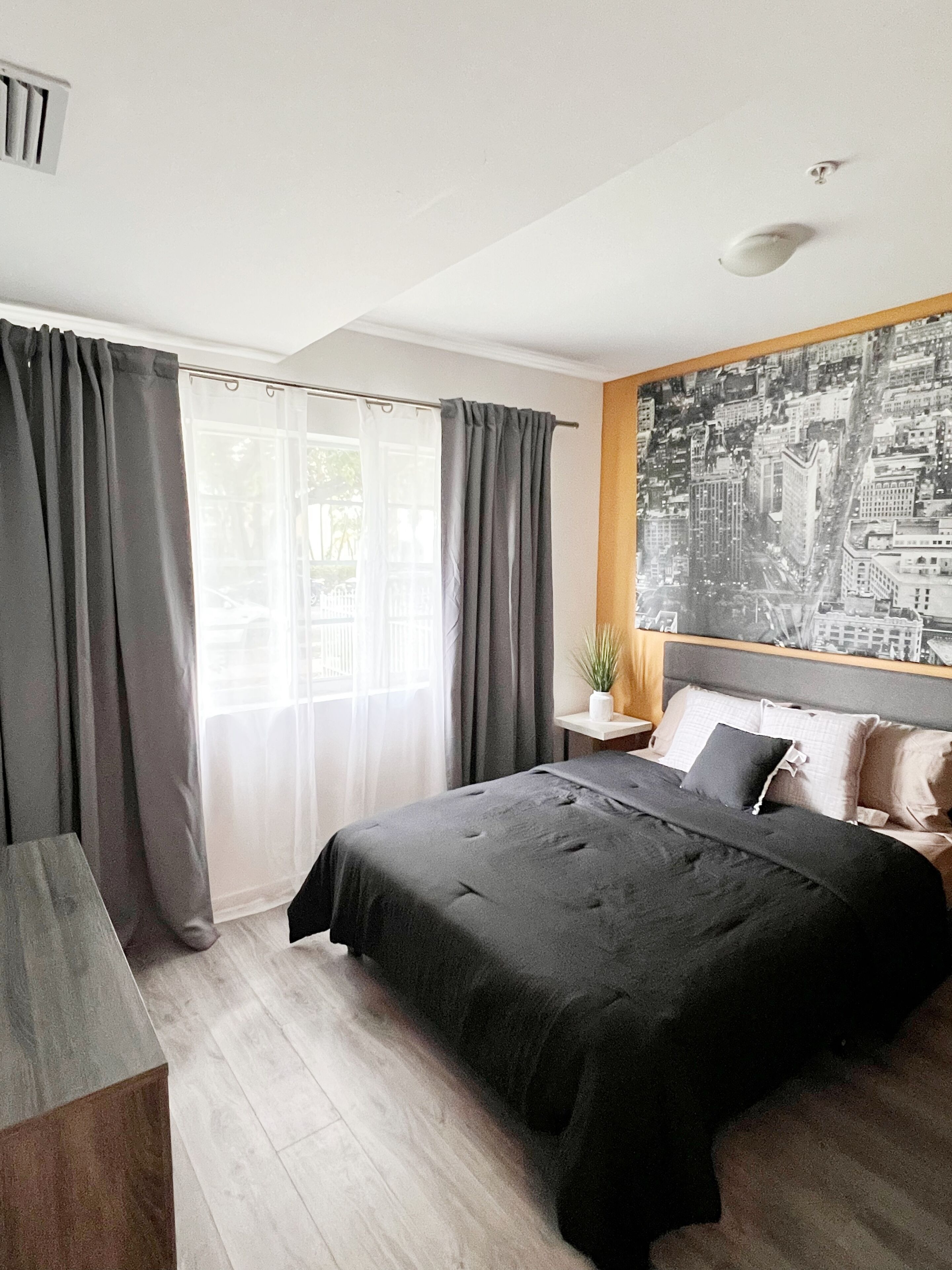 A modern bedroom with a large bed, a cityscape painting, and a window with curtains.