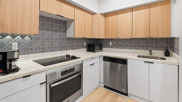 Uma cozinha moderna com armários brancos e de madeira, um painel de backsplash estampado, micro-ondas embutido, cafeteira, forno e lava-louças.