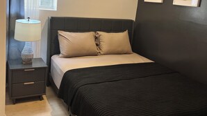 Quarto com cama, mesa de cabeceira, luminária, janela com cortinas e duas obras de arte na parede.