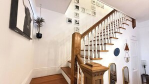Una escalera con barandilla de madera y balaustradas blancas, una planta en maceta y cuadros en la pared.